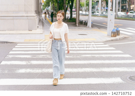 一位年輕女子走過人行道;都市街頭時尚。 一位年輕女子走過人行道;都市街頭時尚。 142710752