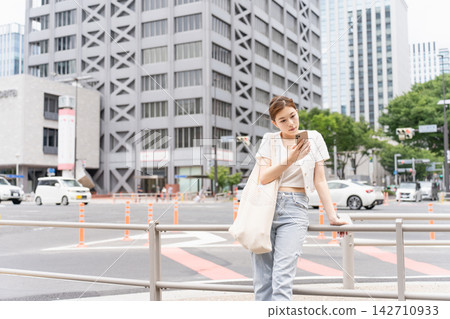 一位穿著休閒的女子在等人時正在查看智慧型手機。 一位穿著休閒的女子在等人時正在查看智慧型手機。 142710933