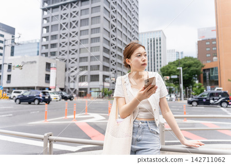 一位穿著休閒的女子在等人時正在查看智慧型手機。 一位穿著休閒的女子在等人時正在查看智慧型手機。 142711062