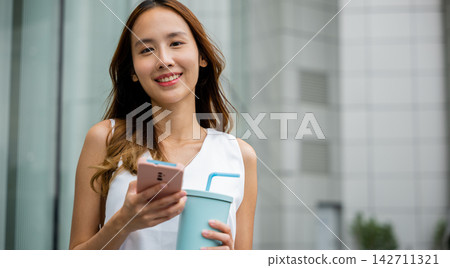 Fashionable woman in white shirt holding a smartphone and a tumbler glass Fashionable woman in white shirt holding a smartphone and a tumbler glass 142711321