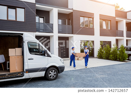 Two removal company workers are loading boxes into a minibus. Two removal company workers are loading boxes into a minibus. 142712657