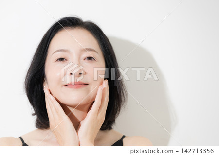 A hilarious beauty portrait of a 50-year-old woman with beautiful skin, showing her skincare routine as she touches her cheek. A hilarious beauty portrait of a 50-year-old woman with beautiful skin, showing her skincare routine as she touches her cheek. 142713356