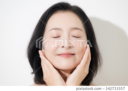 一位50歲、皮膚光滑的女士在美顏照中開懷大笑;她閉上眼睛微笑,用手撫摸臉頰塗抹護膚品。 一位50歲、皮膚光滑的女士在美顏照中開懷大笑;她閉上眼睛微笑,用手撫摸臉頰塗抹護膚品。 142713357