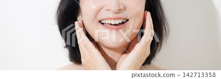 一幅美麗的肖像畫,畫中一位五十多歲的女性肌膚完美無瑕,開懷大笑,用手輕撫臉頰。橫幅圖片:未顯示臉部。 一幅美麗的肖像畫,畫中一位五十多歲的女性肌膚完美無瑕,開懷大笑,用手輕撫臉頰。橫幅圖片:未顯示臉部。 142713358