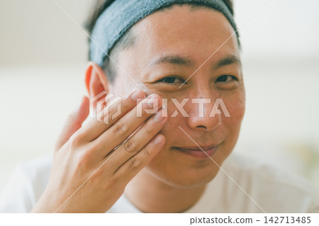 A cheerful man in his 40s enjoying his skincare routine. A cheerful man in his 40s enjoying his skincare routine. 142713485