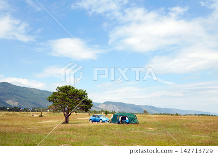 Camping in a large field with a car, tent, tree, and mountains in the background. Camping in a large field with a car, tent, tree, and mountains in the background. 142713729