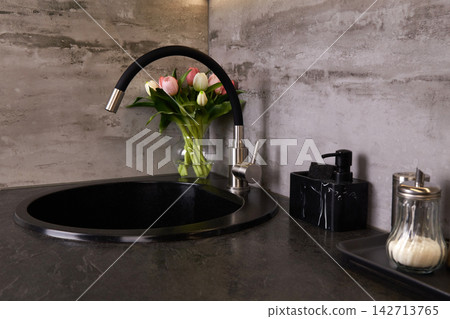 A black circular sink is placed in a kitchen with gray walls. A black circular sink is placed in a kitchen with gray walls. 142713765