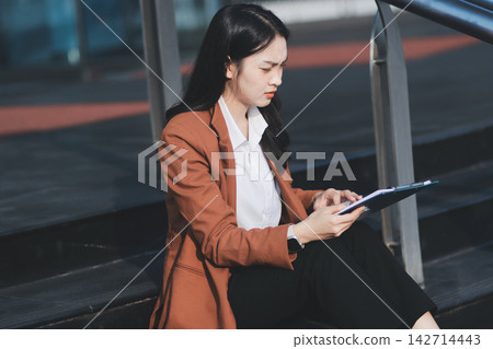 Asian business woman sitting alone on concrete steps, suffering from severe headache, mental stress and deep sadness, contemplating failure after losing her job Asian business woman sitting alone on concrete steps, suffering from severe headache, mental stress and deep sadness, contemplating failure after losing her job 142714443