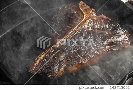 Grilled beef steak with charred surface and smoke rising, placed on a black grill pan, showcasing rich textures and cooking details Grilled beef steak with charred surface and smoke rising, placed on a black grill pan, showcasing rich textures and cooking details 142715001