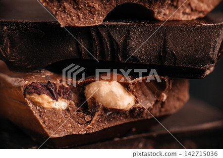 Dark chocolate bars with visible layers of nougat and nuts stacked on a dark surface, showcasing rich textures and contrasting colors Dark chocolate bars with visible layers of nougat and nuts stacked on a dark surface, showcasing rich textures and contrasting colors 142715036