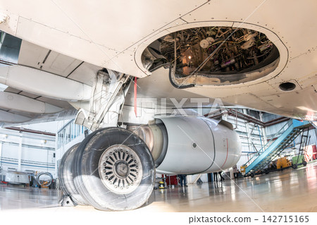 Close-up on the main landing gear of a white passenger airplane and the bottom of the fuselage. The aircraft is serviced in the aviation hangar Close-up on the main landing gear of a white passenger airplane and the bottom of the fuselage. The aircraft is serviced in the aviation hangar 142715165