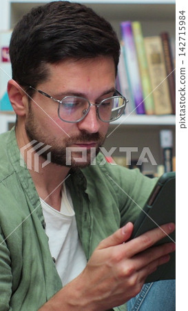 Student using tablet and writing notes in library for class assignment. Student using tablet and writing notes in library for class assignment. 142715984