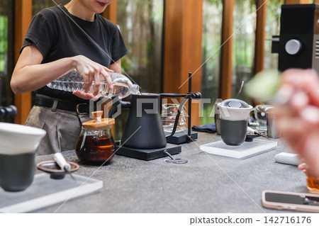 Female barista pouring fresh water from a plastic bottle into an electric gooseneck kettle. 142716176