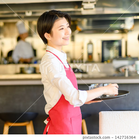 A waitress with a smile holds a tray in the restaurant kitchen. A waitress with a smile holds a tray in the restaurant kitchen. 142716364