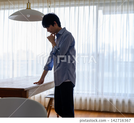 一個男人站在那裡,雙手放在桌上,陷入沉思。 一個男人站在那裡,雙手放在桌上,陷入沉思。 142716367