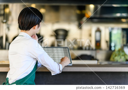 一名店員看著平板電腦,螢幕上顯示櫃檯對面的廚房景象。 一名店員看著平板電腦,螢幕上顯示櫃檯對面的廚房景象。 142716369