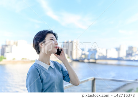 一名女子一邊用智慧型手機通話,一邊抬頭望向天空。 一名女子一邊用智慧型手機通話,一邊抬頭望向天空。 142716378