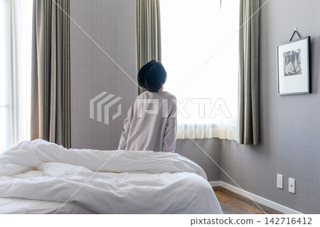 清晨,一位女子在房間裡望著窗外。 清晨,一位女子在房間裡望著窗外。 142716412