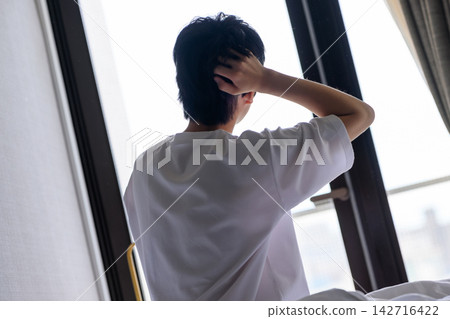 A man runs his hand through his hair by the window. A man runs his hand through his hair by the window. 142716422