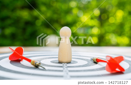 Wooden figure on a dartboard with darts, symbolizing leadership and goal achievement. 142718127