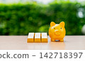 Yellow piggy bank and stack of shiny gold bars on table with green background. 142718397