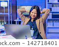 Tired young Asian businesswoman stretching at desk while working on laptop in office. 142718401