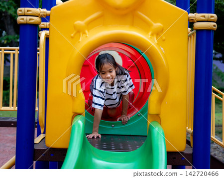 Cute Asian girl crawling out of colorful tunnel tube slide at playground 142720466