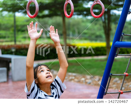 Asian little girl reaching up hands trying to grab gymnastics hanging rings at outdoor playground Asian little girl reaching up hands trying to grab gymnastics hanging rings at outdoor playground 142720467