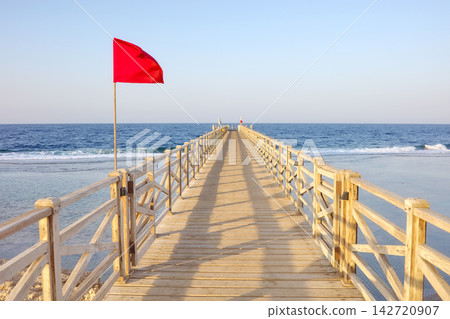 A wooden pier with a red warning flag at sunset. A wooden pier with a red warning flag at sunset. 142720907