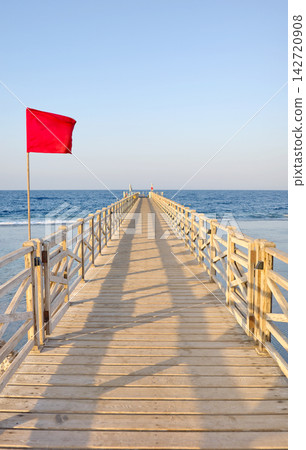 A wooden pier with a red warning flag at sunset. 142720908