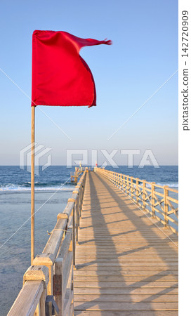 A red warning flag on a wooden pier, selective focus. A red warning flag on a wooden pier, selective focus. 142720909