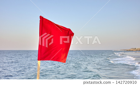 A red warning flag by the sea, selective focus. A red warning flag by the sea, selective focus. 142720910