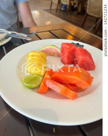 A meal scene featuring a fruit plate with watermelon, pineapple, and papaya, along with forks and knives. A meal scene featuring a fruit plate with watermelon, pineapple, and papaya, along with forks and knives. 142721234