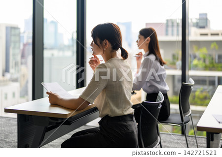 Women listening to a lecture in a conference room with a view of the city from the window. Women listening to a lecture in a conference room with a view of the city from the window. 142721521