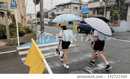 A group of elementary school students walking to school on a rainy day. 142722369