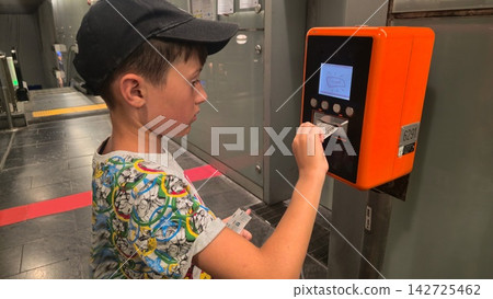 Child uses an automated ticket machine while preparing for a public transport journey. Concepts: independent travel skills, public transit access, transport digitalization, family travel. Child uses an automated ticket machine while preparing for a public transport journey. Concepts: independent travel skills, public transit access, transport digitalization, family travel. 142725462
