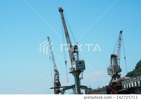 三台造船廠起重機高聳入雲,映襯著淡藍色的天空。 三台造船廠起重機高聳入雲,映襯著淡藍色的天空。 142725711
