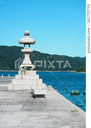 防波堤上矗立著一座石燈籠,碧藍的大海,以及對岸的山脈。 防波堤上矗立著一座石燈籠,碧藍的大海,以及對岸的山脈。 142725720