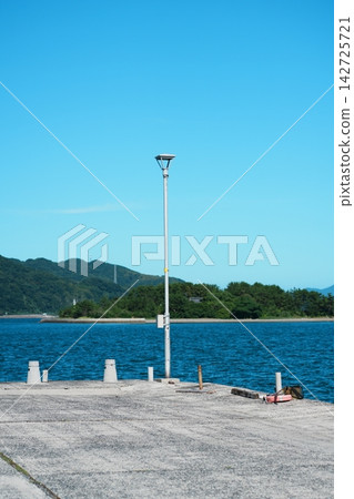 懸崖上的路燈、蔚藍的大海，以及對岸成排的松樹。 142725721