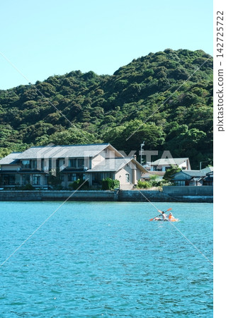 皮划艇漂浮在碧綠的海面上,遠處是海濱村莊。 皮划艇漂浮在碧綠的海面上,遠處是海濱村莊。 142725722