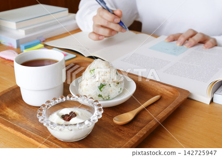A person studying while eating a rice ball and yogurt as a late-night snack. A person studying while eating a rice ball and yogurt as a late-night snack. 142725947