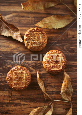 Traditional mooncakes with intricate designs placed on a wooden surface, surrounded by dried leaves, symbolizing the Mid-Autumn Festival celebration Traditional mooncakes with intricate designs placed on a wooden surface, surrounded by dried leaves, symbolizing the Mid-Autumn Festival celebration 142726683
