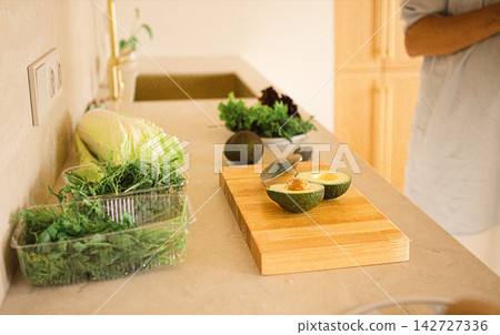 Fresh vegetables and avocados on a wooden cutting board in a modern kitchen with a minimalist design and natural light illuminating the countertop Fresh vegetables and avocados on a wooden cutting board in a modern kitchen with a minimalist design and natural light illuminating the countertop 142727336