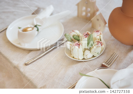 Elegant table setting featuring decorative food art resembling flowers, with white plates, cutlery, and a clay pot in a soft, neutral-toned dining environment Elegant table setting featuring decorative food art resembling flowers, with white plates, cutlery, and a clay pot in a soft, neutral-toned dining environment 142727338
