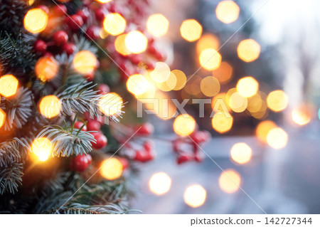 Close-up of evergreen branches adorned with red berries and warm glowing lights, creating a festive atmosphere during the holiday season Close-up of evergreen branches adorned with red berries and warm glowing lights, creating a festive atmosphere during the holiday season 142727344