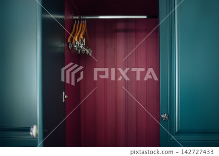 Interior view of a modern wardrobe with teal doors, featuring wooden hangers and a deep red interior, showcasing a stylish and organized storage solution Interior view of a modern wardrobe with teal doors, featuring wooden hangers and a deep red interior, showcasing a stylish and organized storage solution 142727433