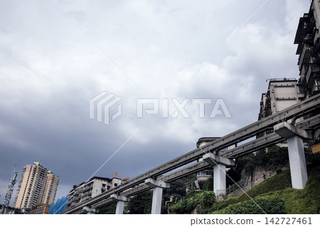 Urban landscape featuring elevated monorail system traversing through residential buildings under a cloudy sky in a modern city setting Urban landscape featuring elevated monorail system traversing through residential buildings under a cloudy sky in a modern city setting 142727461