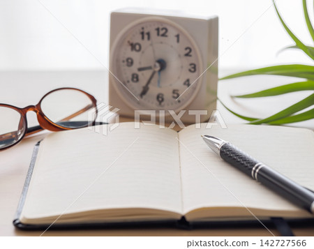 A wooden desk with a notebook and pen, glasses and a watch on it. A wooden desk with a notebook and pen, glasses and a watch on it. 142727566