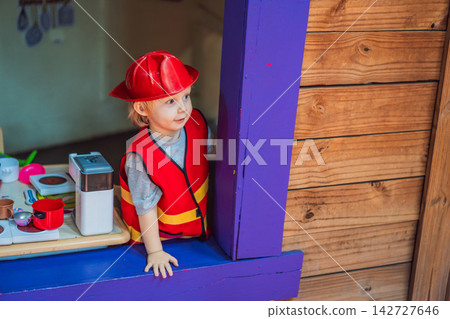 Little boy dressed as firefighter playing in a red toy fire truck at an outdoor playground with helmet safety vest pretend rescue game childhood dreams role play and near viewpoint. Little boy dressed as firefighter playing in a red toy fire truck at an outdoor playground with helmet safety vest pretend rescue game childhood dreams role play and near viewpoint. 142727646
