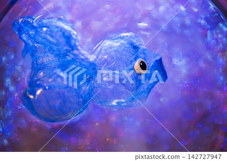 Blue plastic fish sculpture made from recycled materials, floating in water with colorful bokeh background, representing environmental awareness and ocean conservation Blue plastic fish sculpture made from recycled materials, floating in water with colorful bokeh background, representing environmental awareness and ocean conservation 142727947
